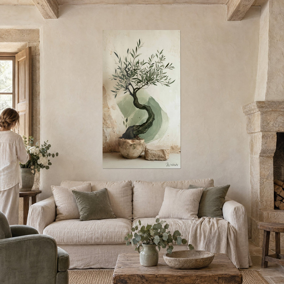 Wall art olive tree with a sage green, twisted trunk on beige background, fine foliage, woman seen from behind, above a sofa in a bright living room