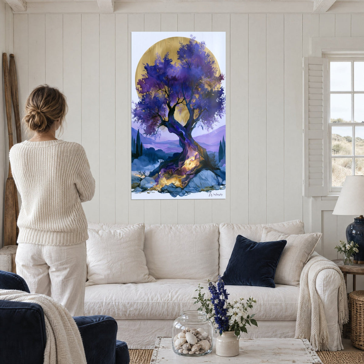Wall art gnarled olive tree with violet foliage in front of a golden disc, person seen from behind, above a sofa in a bright living room