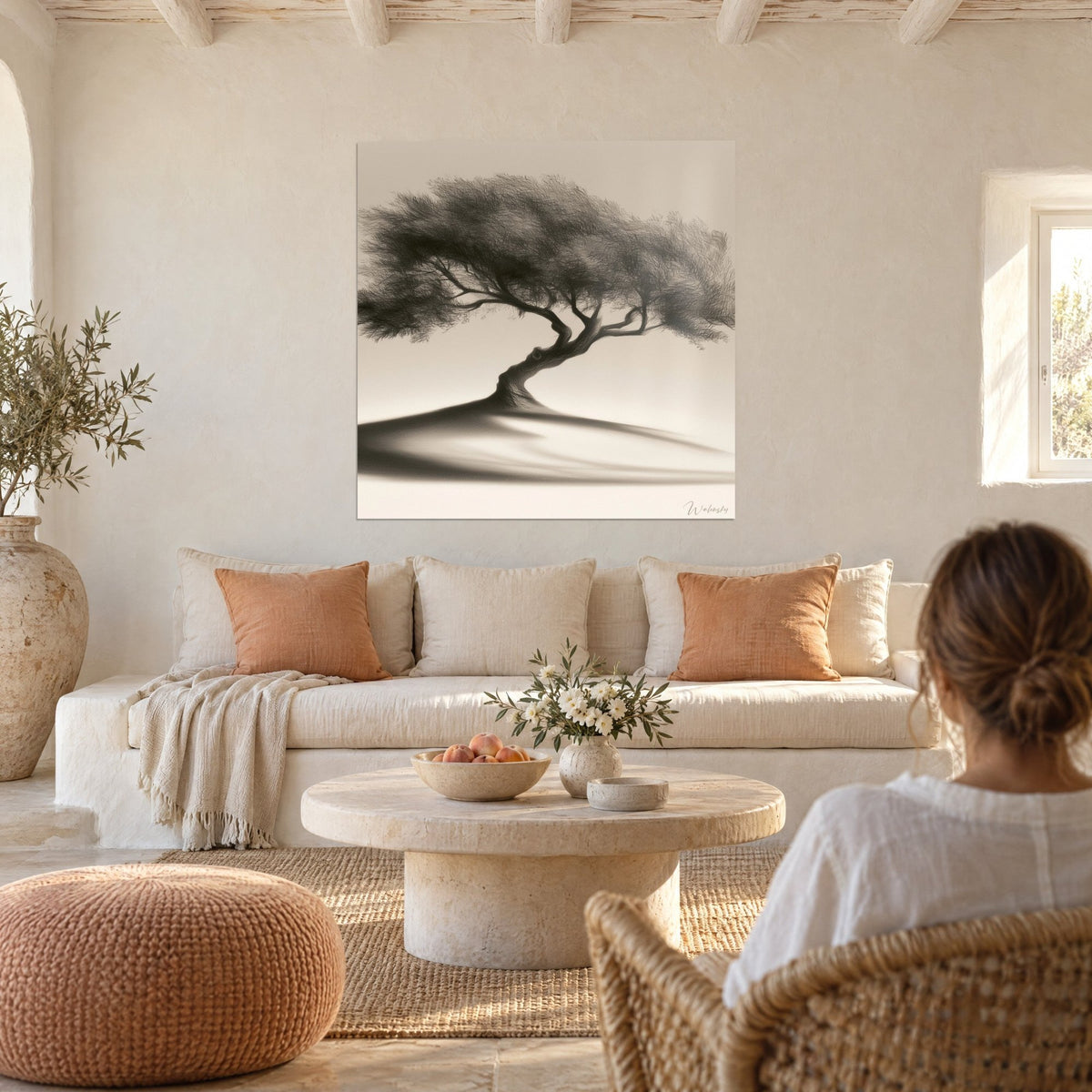 Wall art of a black olive tree with charcoal foliage on a beige hill, ochre and cream, above a sofa in a bright living room