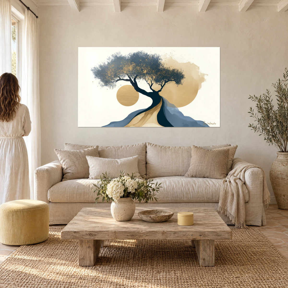 Wall art stylized olive tree with slate-blue foliage flecked with gold, golden sun, woman seen from behind, above a sofa in a bright living room