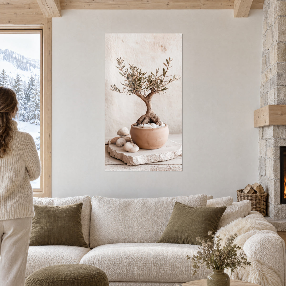 Tableau olivier bonsaï au tronc noueux brun dans un pot terre cuite, galets beiges, au-dessus d'un canapé dans un salon lumineux