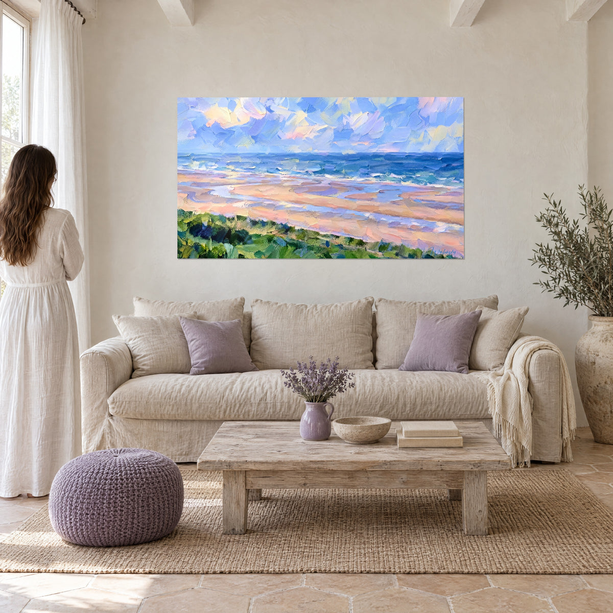 Tableau plage au sable rose et vagues bleues, ciel de nuages lilas et jaune pâle, au-dessus d'un canapé dans un salon lumineux