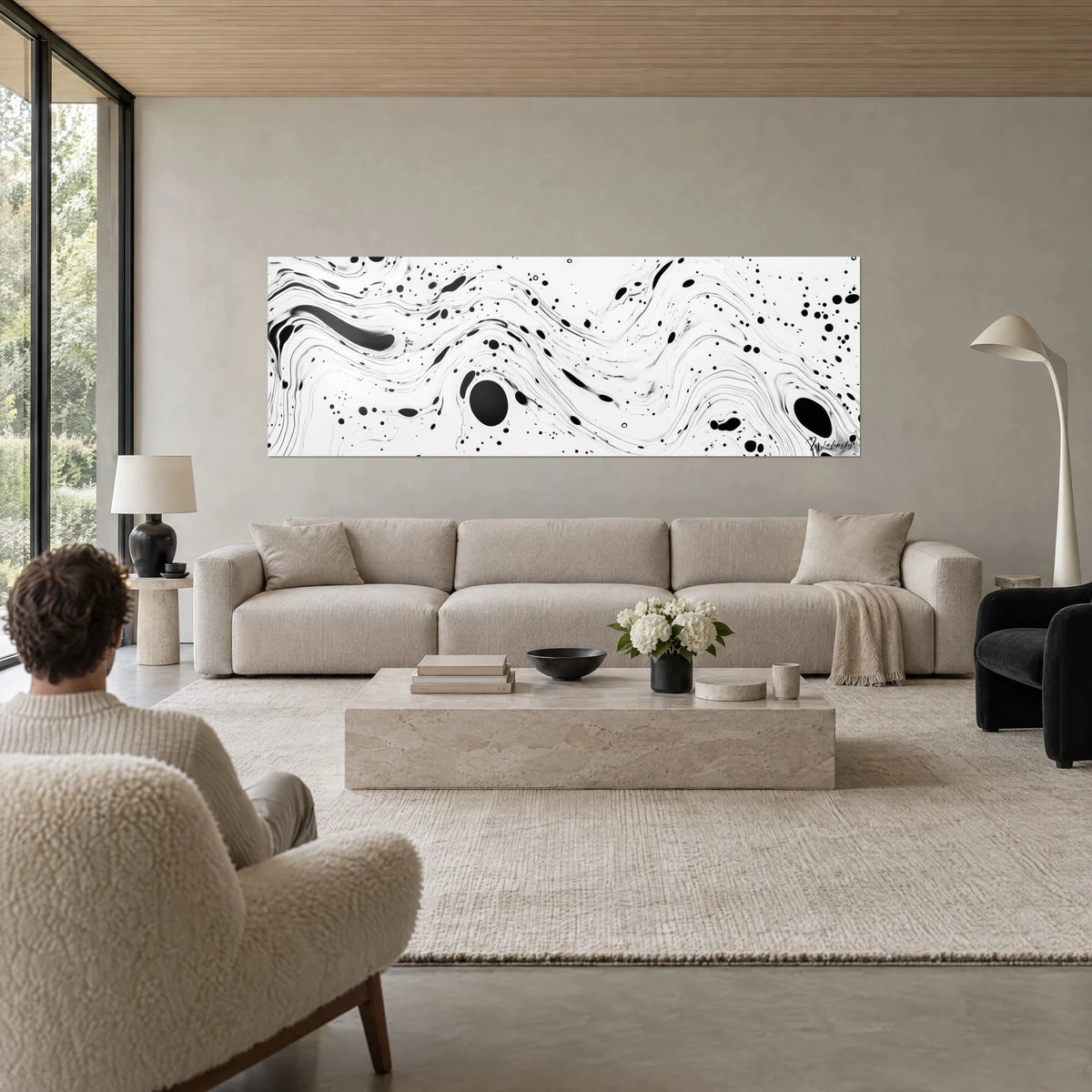 Wall art with flowing black ink currents undulating on a white background, scattered spots and bubbles, above a sofa in a bright living room