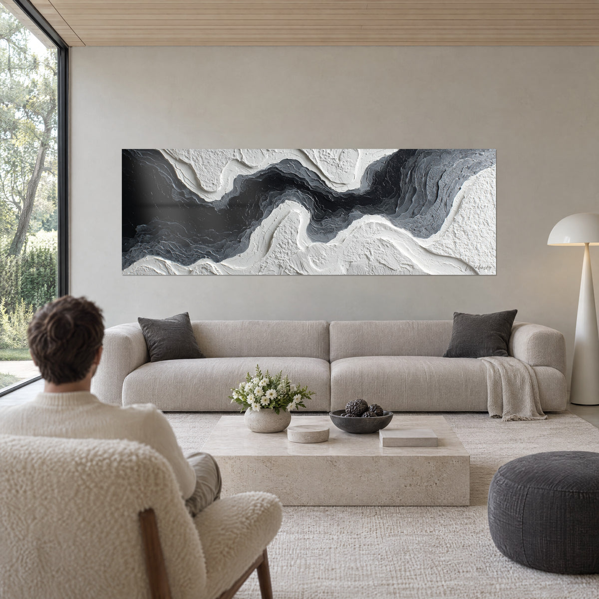 Cuadro de un río oscuro esculpido en relieve blanco y gris, vista de espaldas, sobre un sofá en un salón luminoso