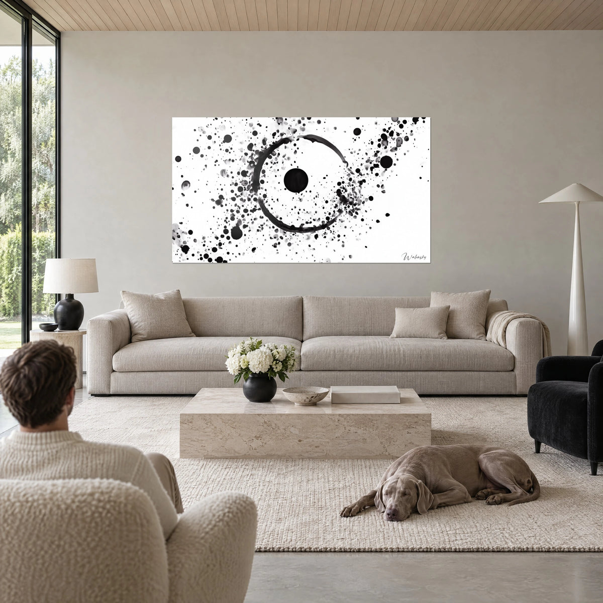 Gemälde Tintenring mit schwarzen Spritzern auf weißem Grund, schwarzer Mittelpunkt, über einem Sofa in einem hellen Wohnzimmer