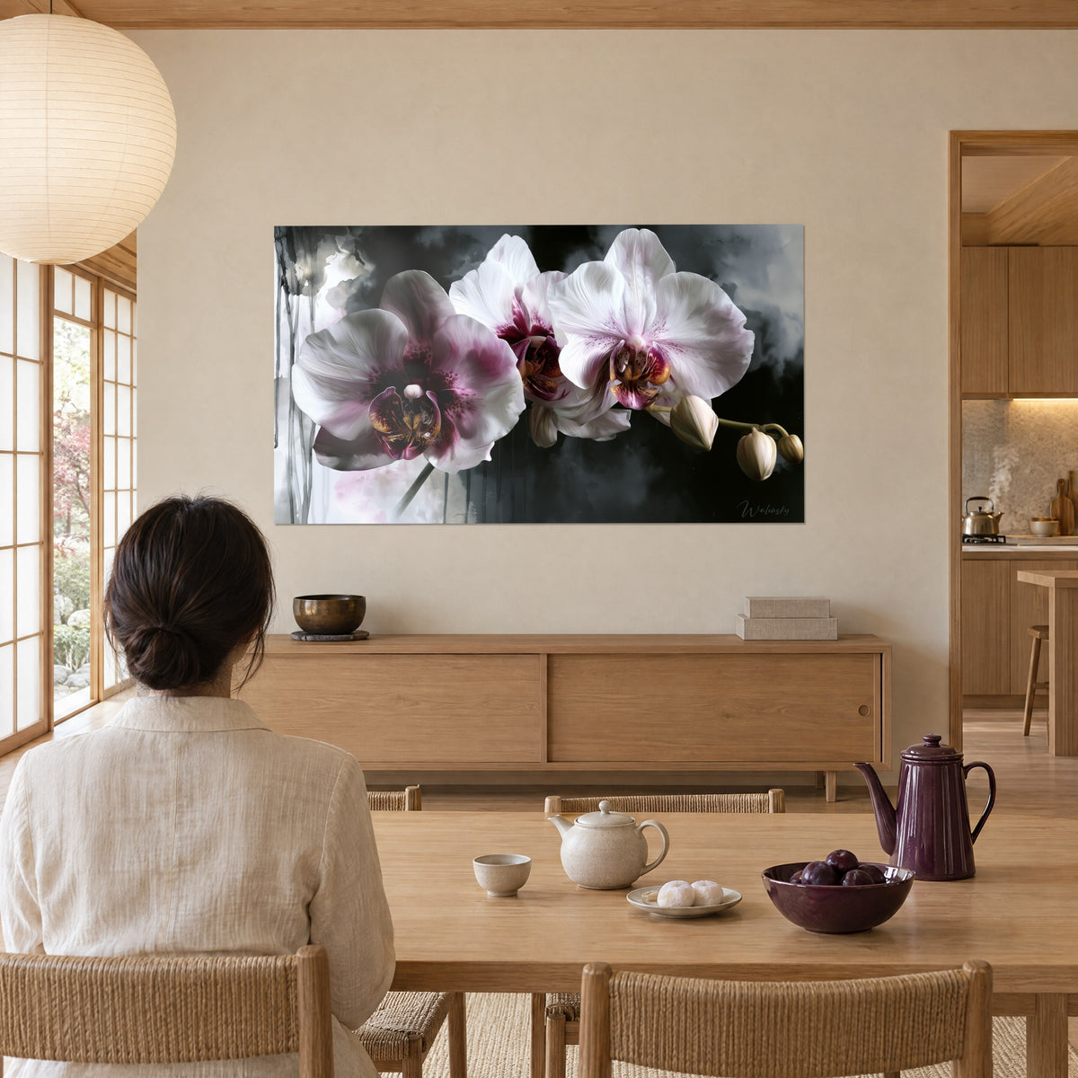 Cuadro flores de orquídea rosa pálido con labelo dorado, nubes grises y goteos, frente a una mujer de espaldas sentada a la mesa de madera