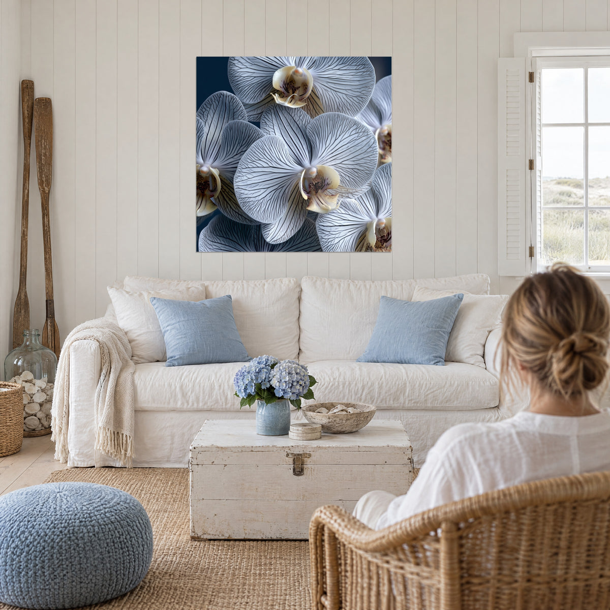 Cuadro de orquídeas blancas con nervaduras antracita sobre fondo azul noche, mujer de espaldas, sobre un sofá en un salón luminoso