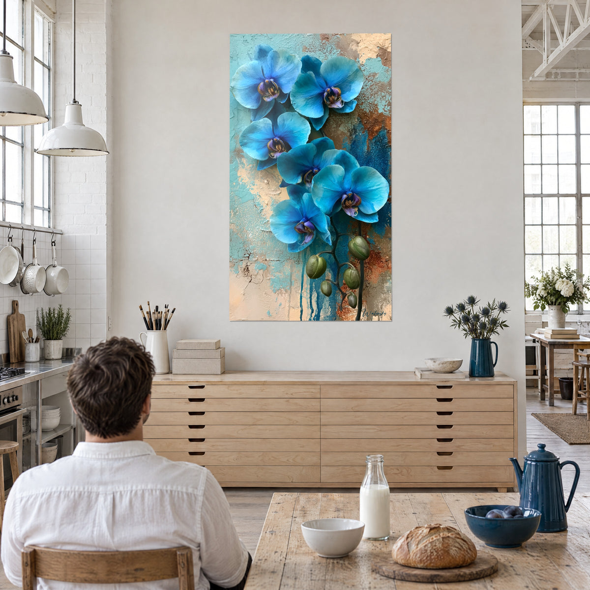 Gemälde mit einem Strauß lagunenblauer Orchideen auf strukturiertem Ocker, ein Mann von hinten am Tisch, offene Küche eines lichtdurchfluteten Lofts