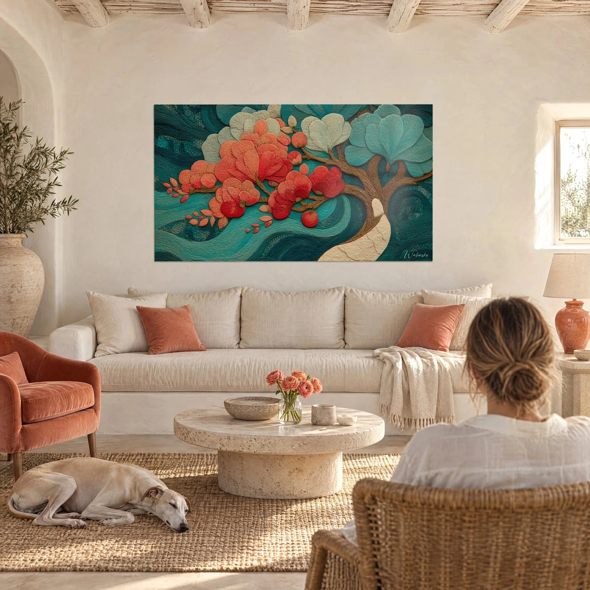 Gemälde Orchideen in Korallenrot mit gestickten Blütenblättern auf türkisfarbenen Wellen, betrachtet von einer Frau von hinten und einem Windhund, über einem Sofa in einem hellen Wohnzimmer