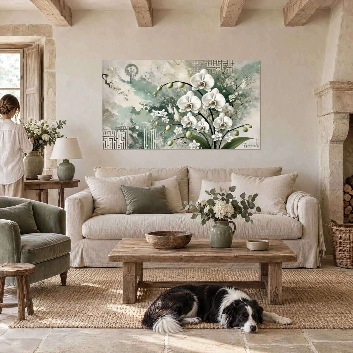 Gemälde weiße Orchideen mit ockerfarbenem Herz auf salbeigrünem Grund, Frau von hinten und schwarz-weißer Collie, über einem Sofa in einem hellen Wohnzimmer