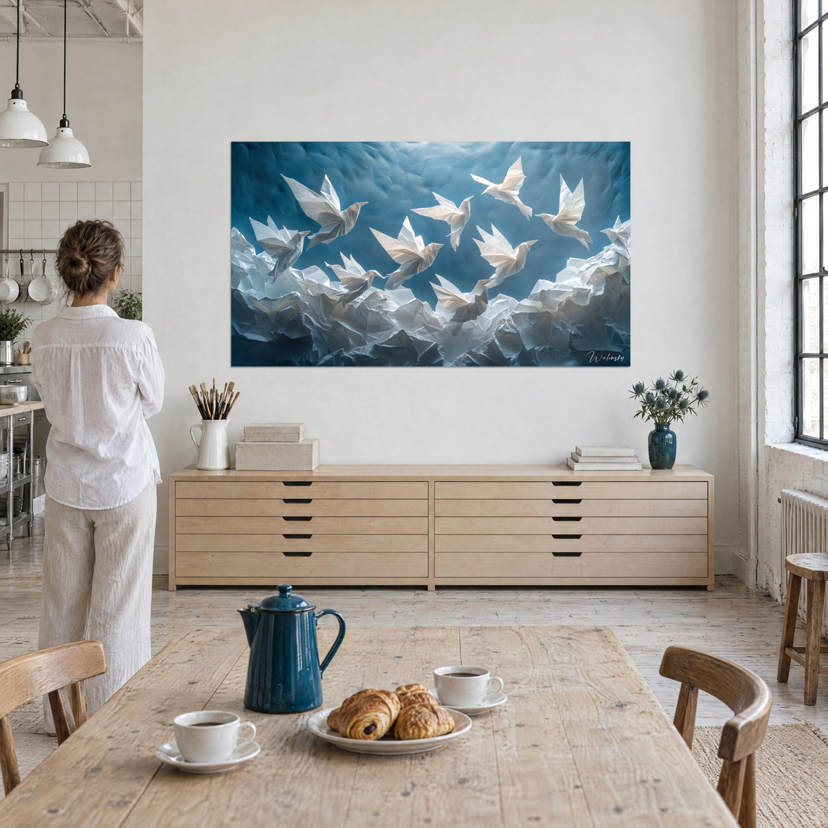 Tableau volée de colombes en papier plié, blanc nacré sur bleu glacier, observée par une femme de dos dans un loft d'artiste