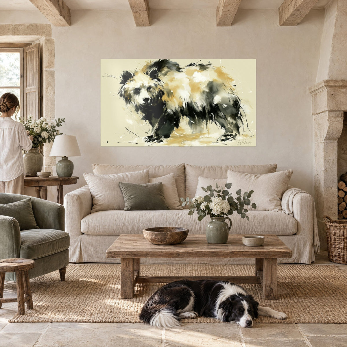 Schilderij grote beer in ocker- en antracietkleurige vlakken, waakzame blik, vrouw van achteren en collie, boven een bank in een lichte woonkamer
