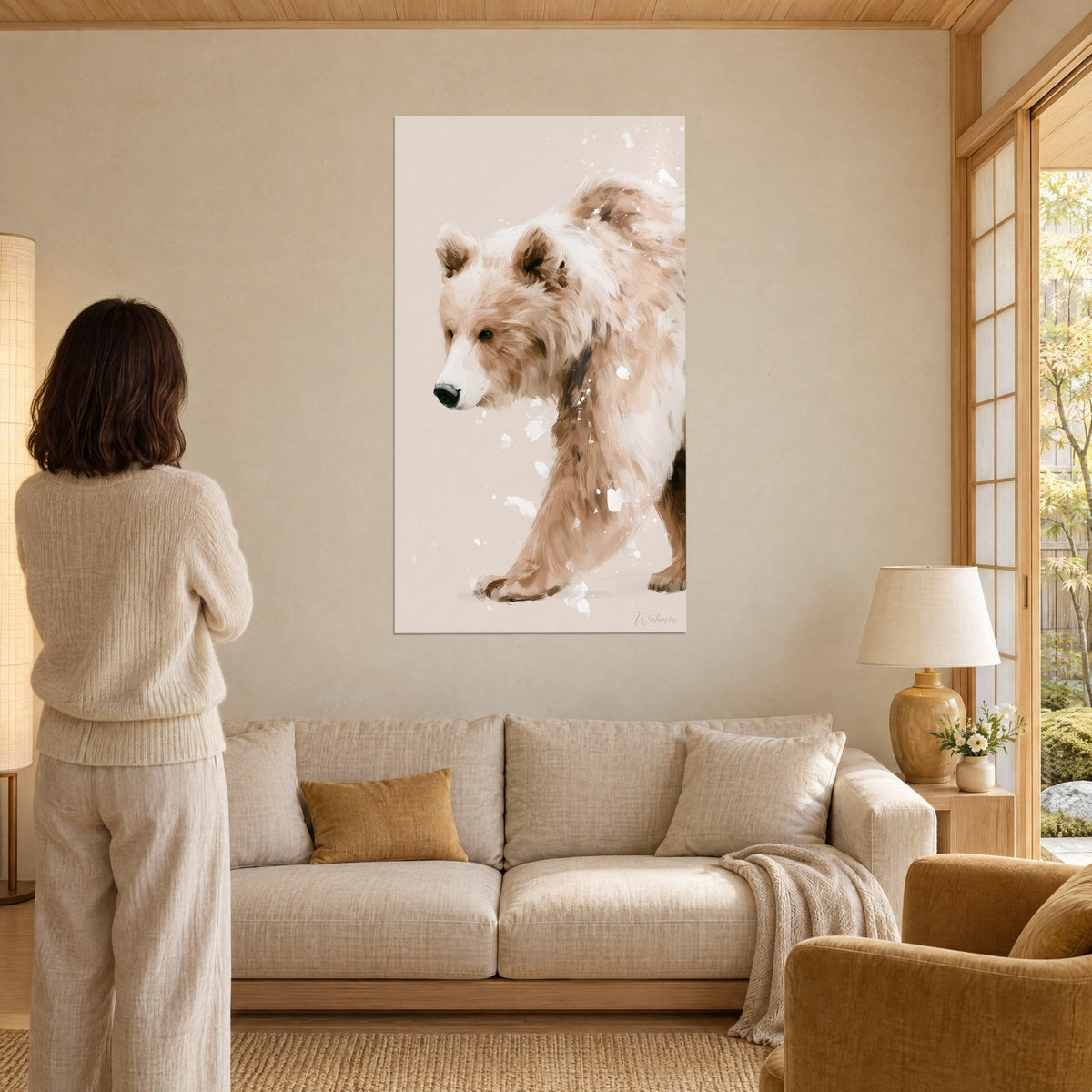 Gemälde Braunbär auf dem Weg, beige und weiß gesprenkeltes Fell mit Schneeflecken vor rosafarbenem Hintergrund, Frau von hinten, über einem Sofa in einem hellen Wohnzimmer