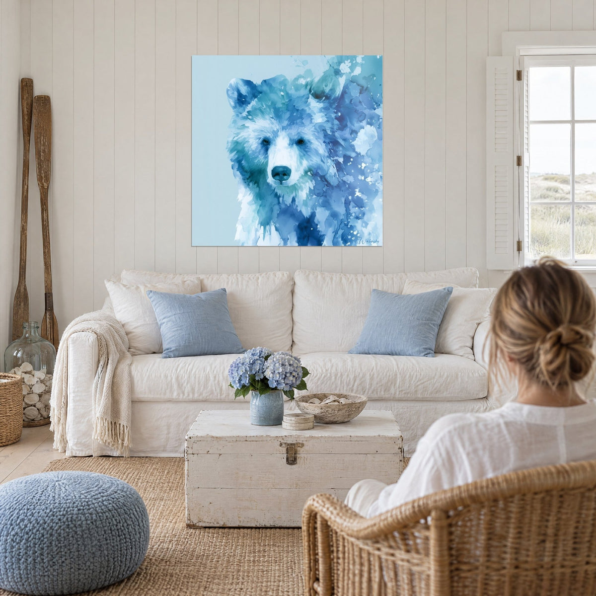 Gemälde Bär im Aquarell in Kobaltblau und Weiß, eine Frau von hinten blickt darauf über einem Sofa in einem hellen Wohnzimmer