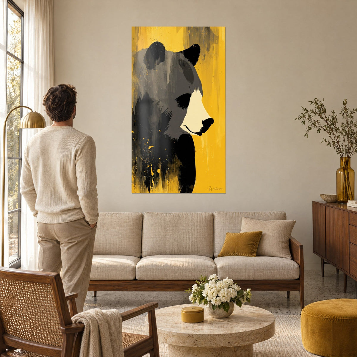 Wall art brown bear in flat anthracite tones, cream muzzle and flowing mustard-yellow background, man seen from behind above a sofa in a bright living room