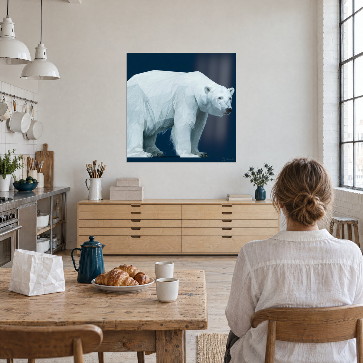 Tableau seigneur des glaces en aplats blanc et gris perle, fond marine, contemplé par une femme de dos dans un loft clair, croissants sur la table