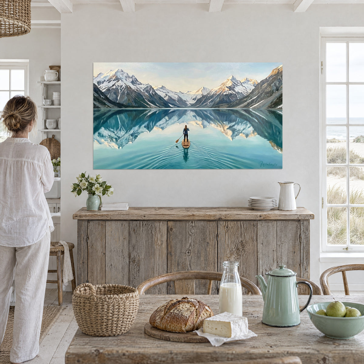 Tableau rameuse debout sur sa planche, montagnes poudrées de neige et eau turquoise, mur blanc lambrissé près d'une fenêtre, bord de mer