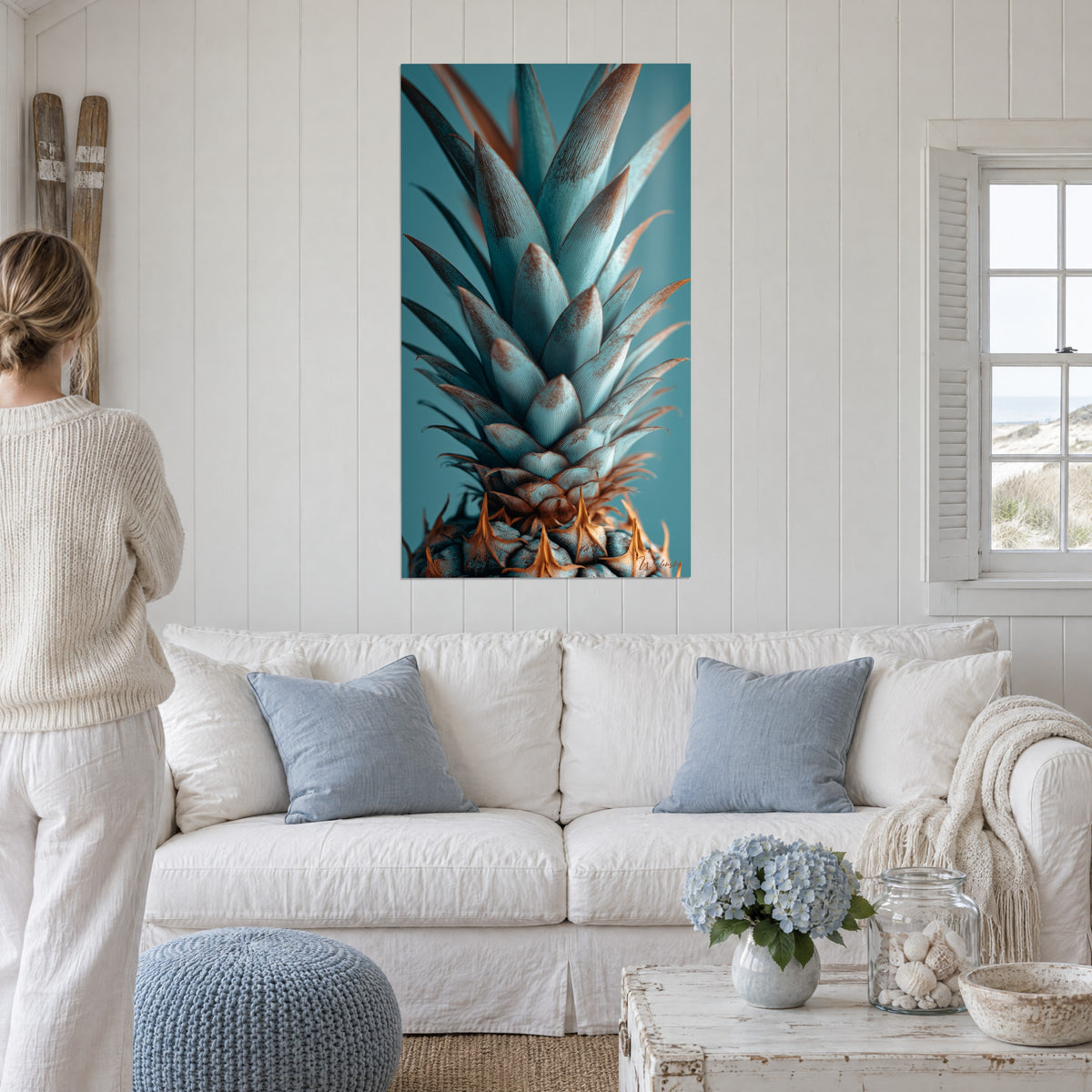Tableau couronne d'ananas turquoise aux pointes cuivrées, au-dessus d'un canapé dans un salon lumineux