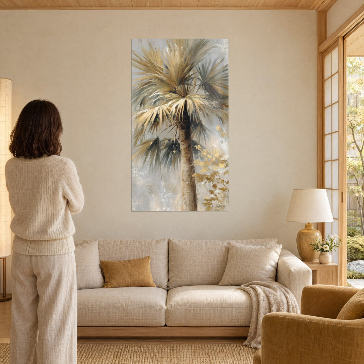 Wall art palm tree with ivory and grey-green fronds, golden highlights, woman seen from behind, above a sofa in a bright living room