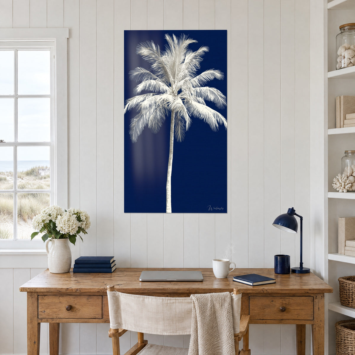 Tableau cocotier crème aux folioles effilées sur fond marine, bureau en bois, lampe bleu nuit et bouquet blanc, étagère de coquillages