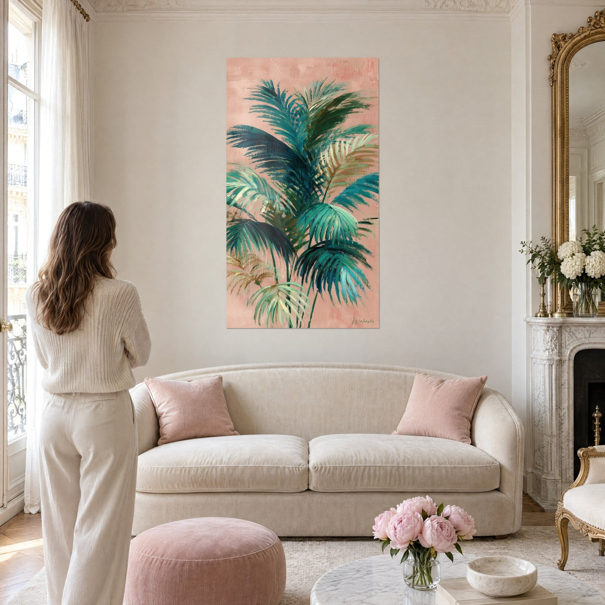 Schilderij palmboom met dennengroene en turquoise bladeren op poederroze achtergrond, vrouw van achteren, boven een bank in een lichte woonkamer