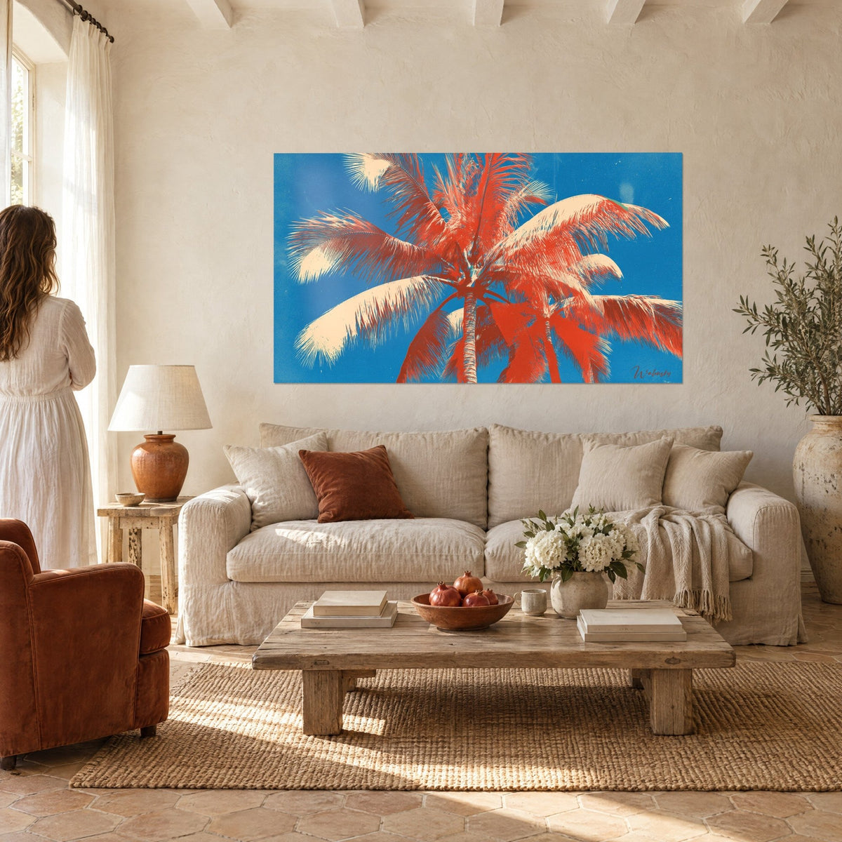 Schilderij rode korallen palmboom tegen azuurblauwe lucht, grote crèmekleurige franjes, vrouw van achteren, boven een bank in een lichte woonkamer
