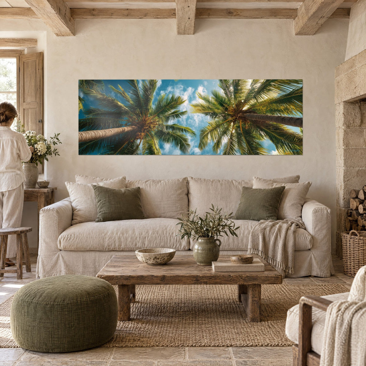 Wall art coconut palms seen from below, brown trunks and green fronds against a blue sky, above a sofa in a bright living room