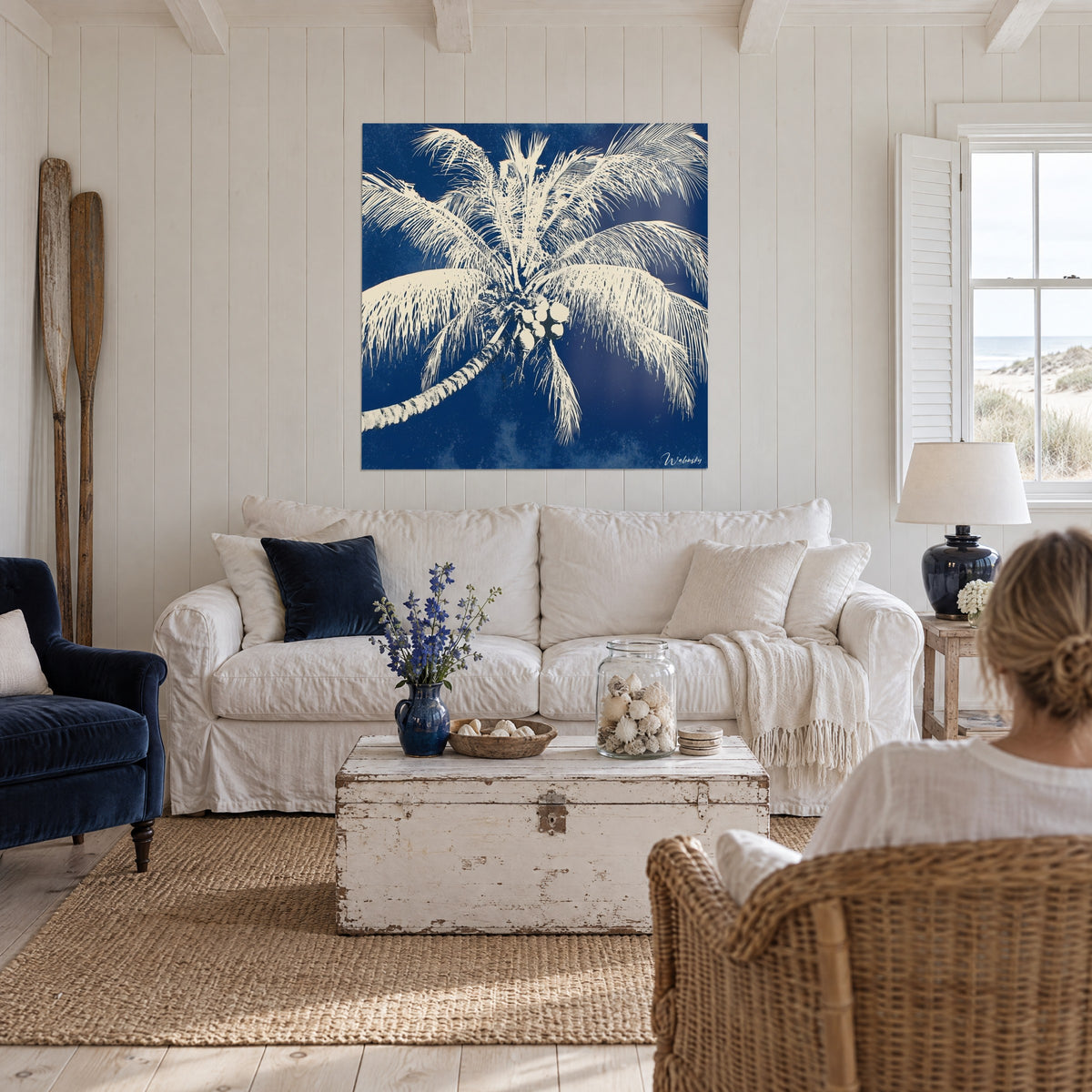 Wall art profile palm tree in navy blue and cream white, cluster of coconuts at the center, above a sofa in a bright living room
