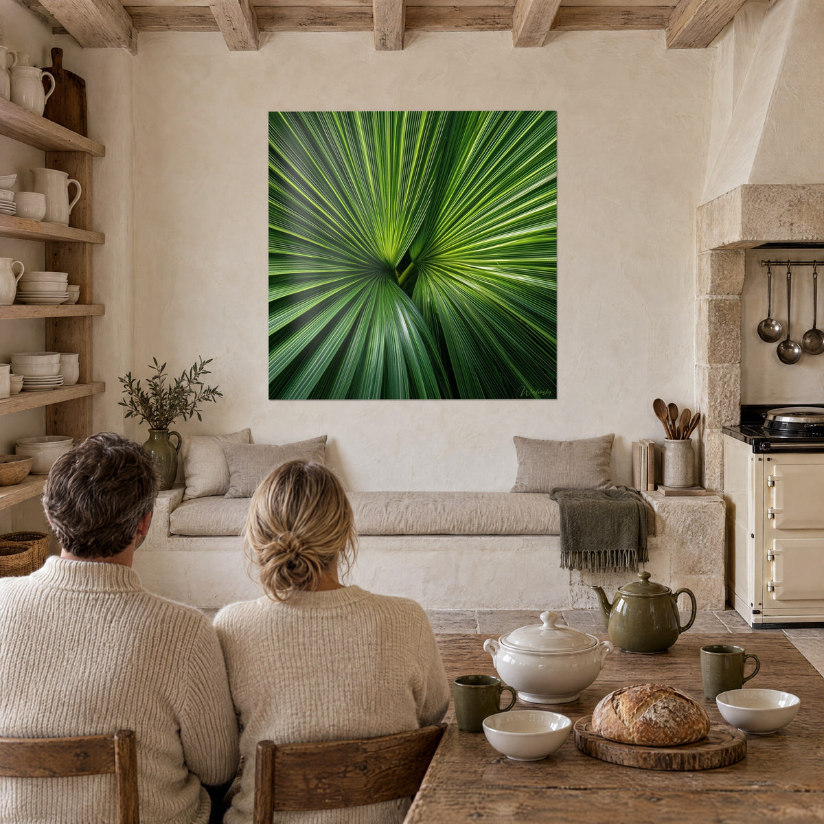 Schilderij palmbladeren in een bundel, zachte groene en felgele strepen, twee vrouwen van achteren aan tafel in een stenen keuken