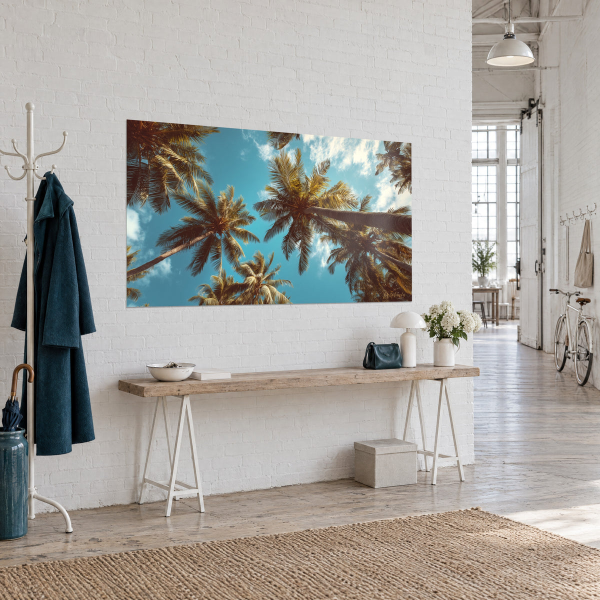 Wall art coconut palms with leaning trunks, turquoise blue sky and golden brown fronds, on a white wall in an artist's loft