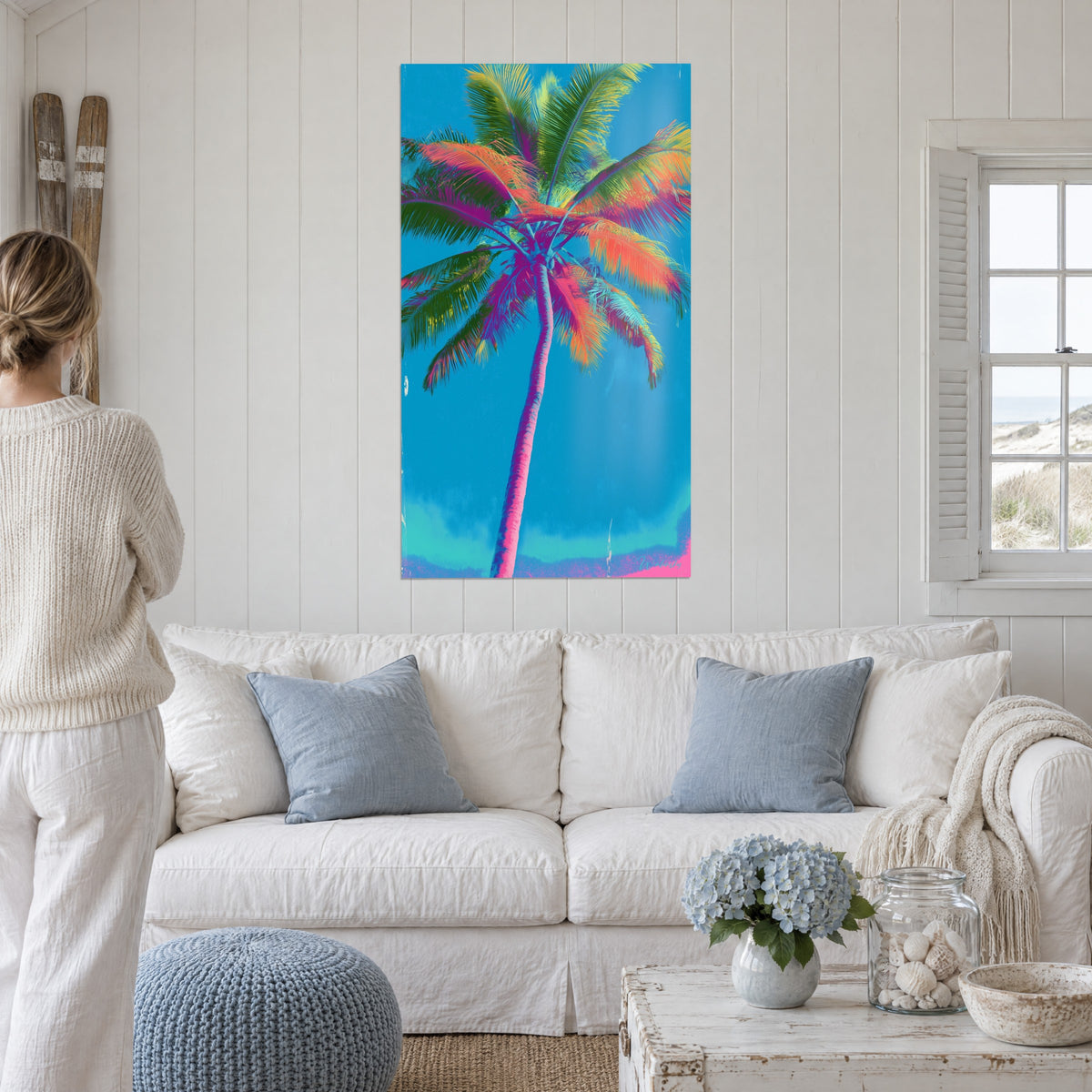 Quadro palma dal tronco rosa e fronde arancioni, verdi e viola su cielo turchese, sopra un divano in un soggiorno luminoso