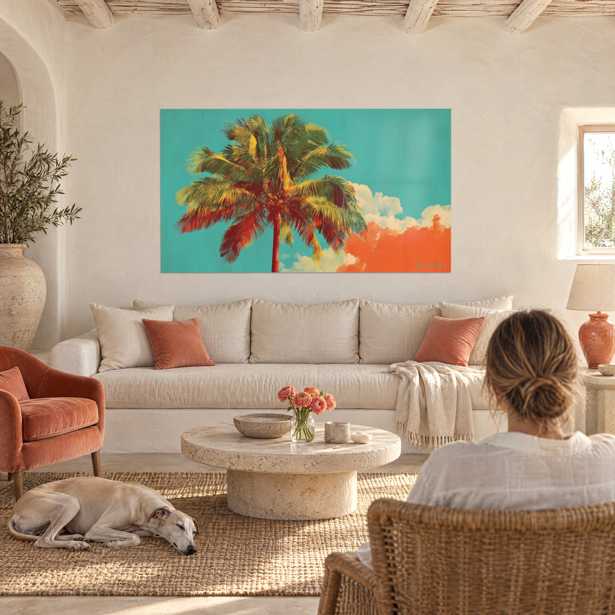 Wall art tropical palm tree with red and yellow fronds against a turquoise sky, couple seen from behind and a greyhound, above a sofa in a bright living room