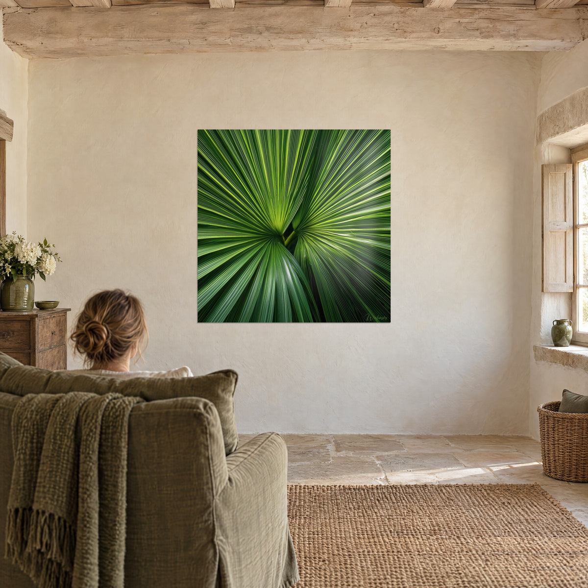 Schilderij palmuitbarsting in jadegroene en bleekgele stralen, een vrouw van achteren in een olijfgroene fauteuil, beige muur en steen