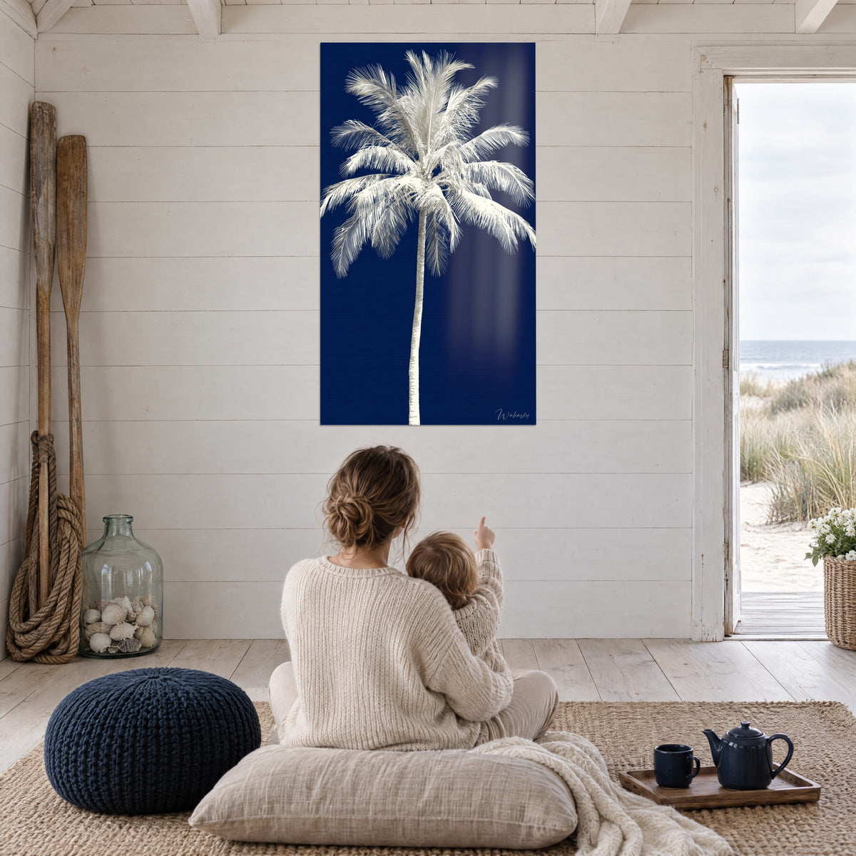 Tableau grand palmier d'ivoire sur nuit bleue, mère et bébé de dos assis sur coussins beiges, porte ouverte sur la plage
