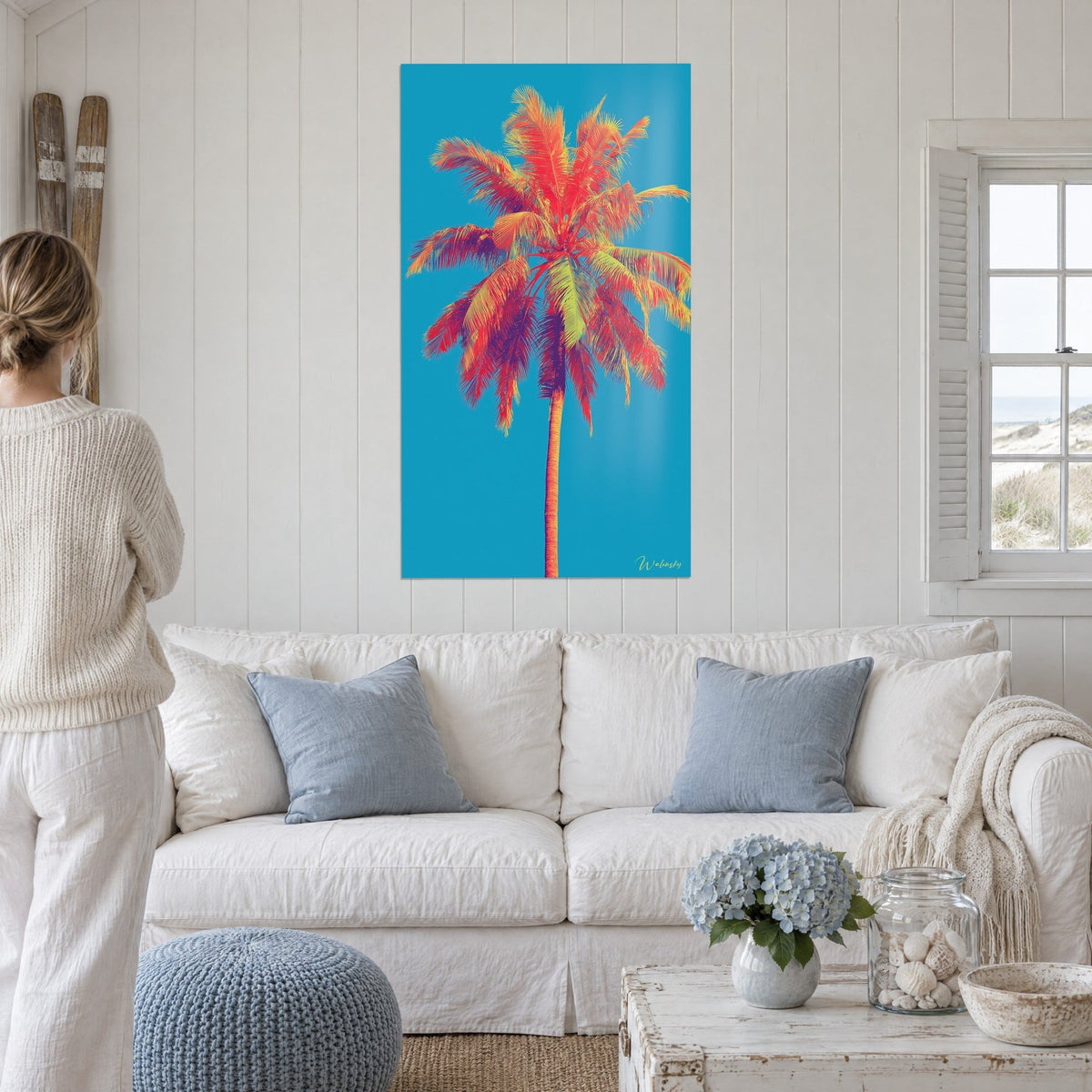 Quadro palma da cocco con foglie rosso corallo e gialle, tronco arancio su cielo turchese, sopra un divano in un soggiorno luminoso