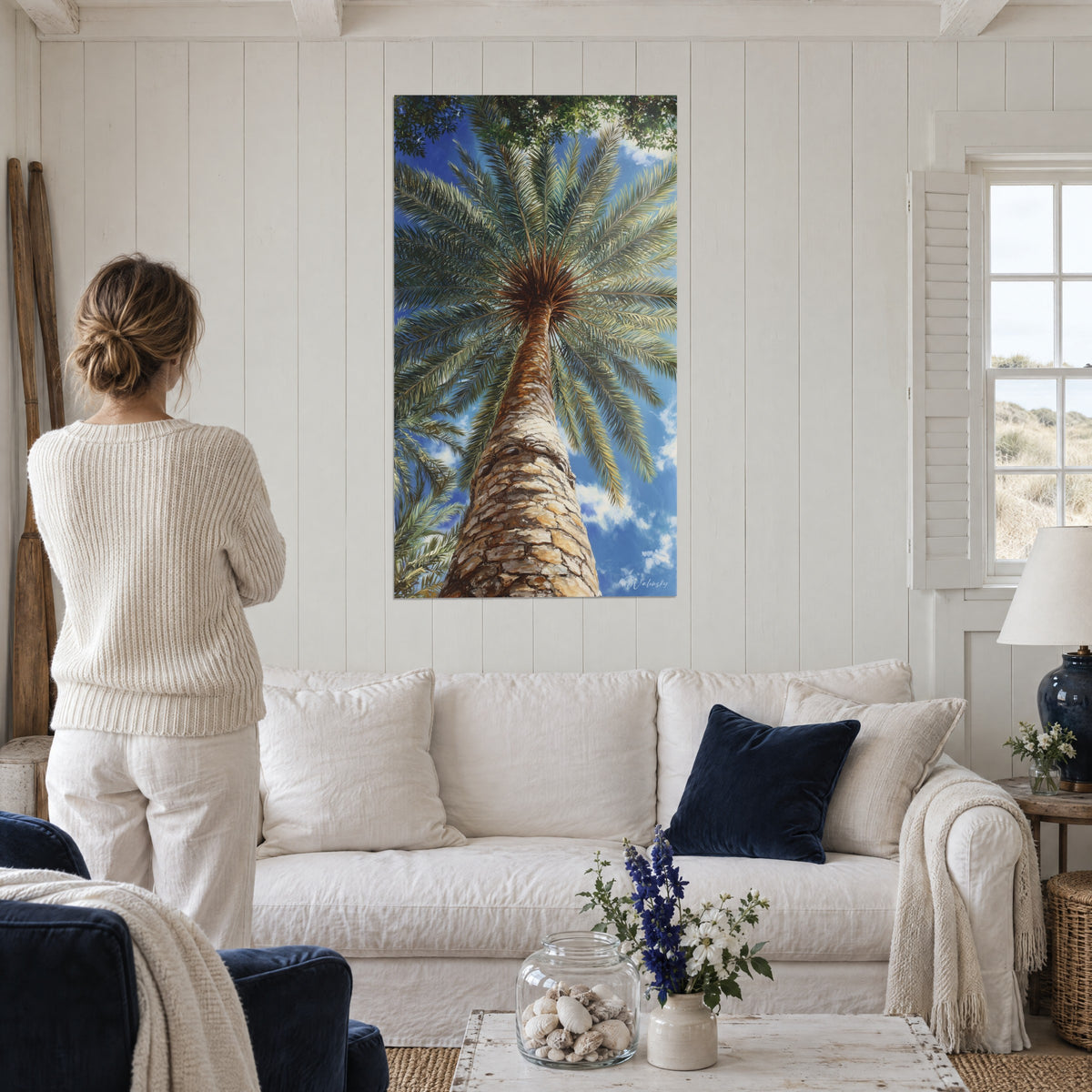 Tableau palmier dattier vu du sol, tronc écorcé beige et ocre, palmes vertes sur ciel bleu, au-dessus d'un canapé dans un salon lumineux