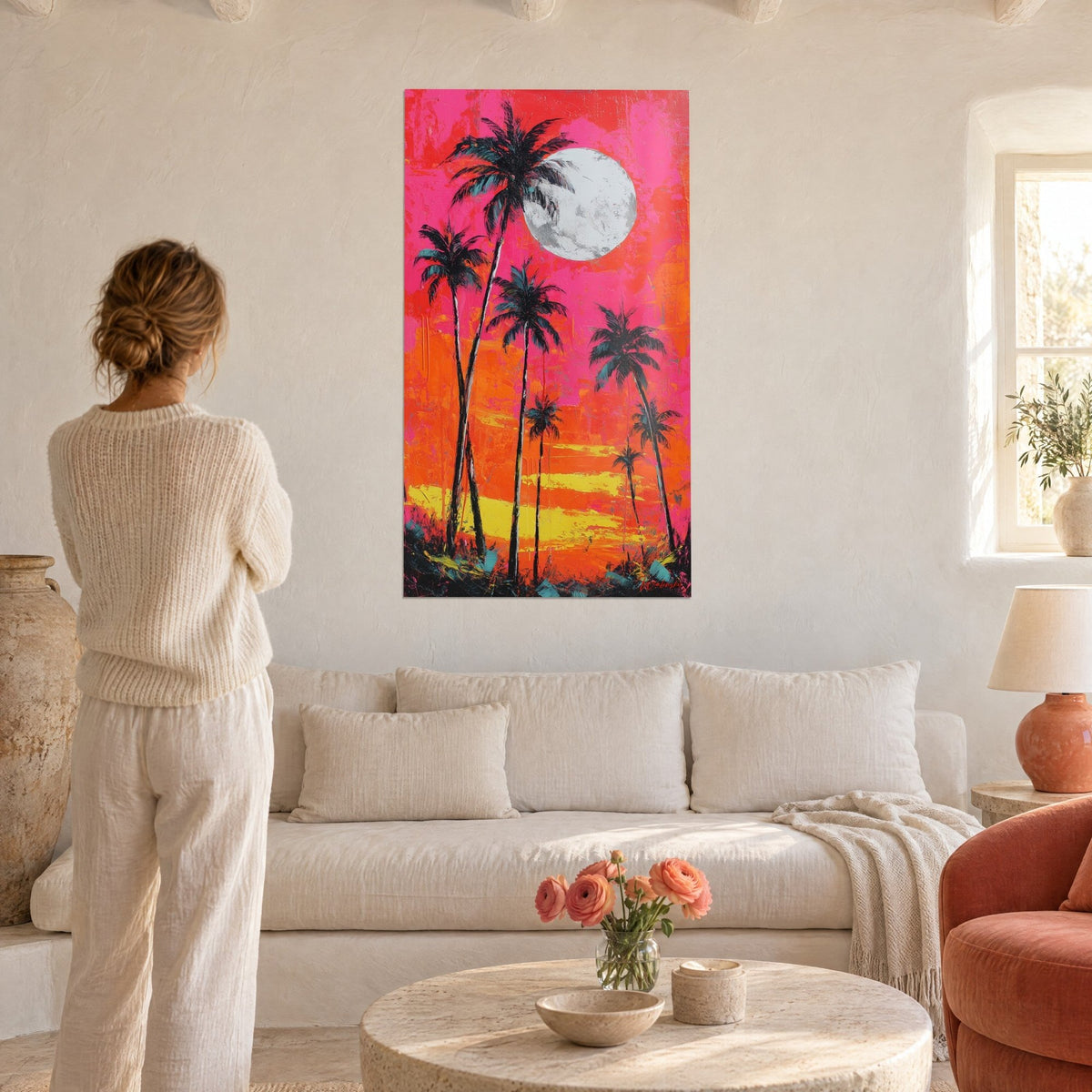 Wall art black palms with turquoise fronds under a white moon, pink and orange sky, woman seen from behind, above a sofa in a bright living room