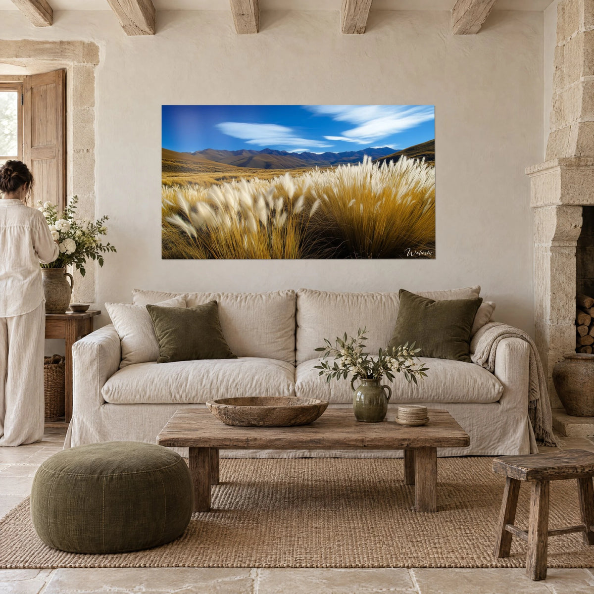 Cuadro de hierba de la pampa con plumeros crema bajo un cielo azul intenso, montañas violetas, encima de un sofá en un salón luminoso