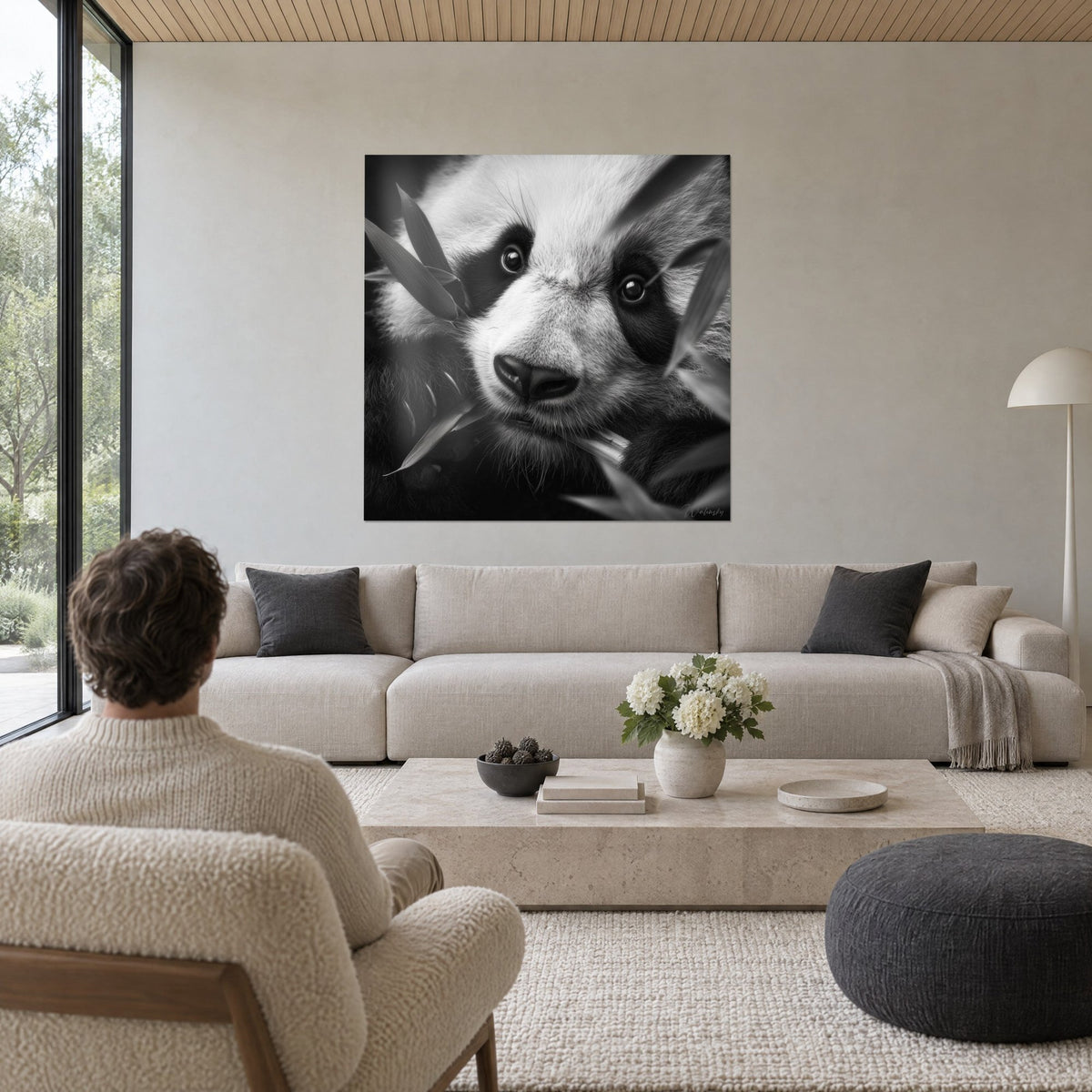Wall art young panda with bright eyes ringed in black, white fur and grey bamboo leaves, above a sofa in a bright living room