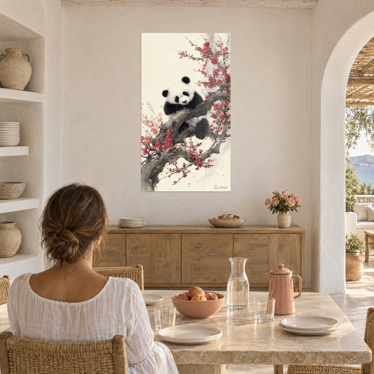 Schilderij reusachtige panda met zwarte vlekken in een roze en rode pruimenboom, crèmekleurige achtergrond, vrouw van achteren aan tafel, Mediterraans interieur met bogen
