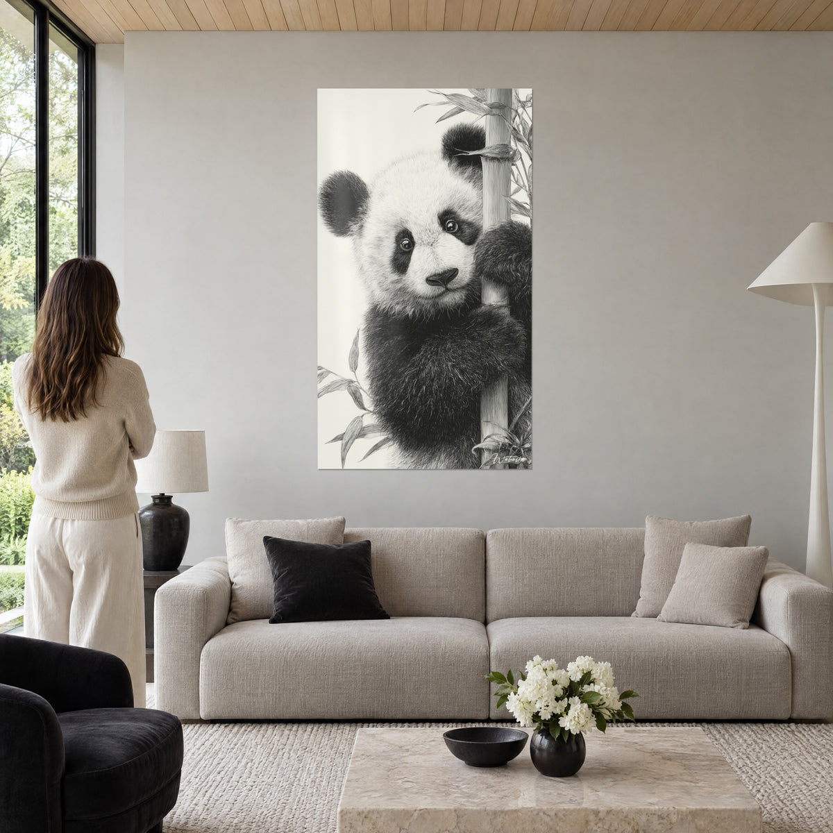 Πίνακας panda αρκουδάκι με ατημέλητη ασπρόμαυρη γούνα, αγκαλιάζει ένα μπεζ μπαμπού, πάνω από καναπέ σε φωτεινό σαλόνι