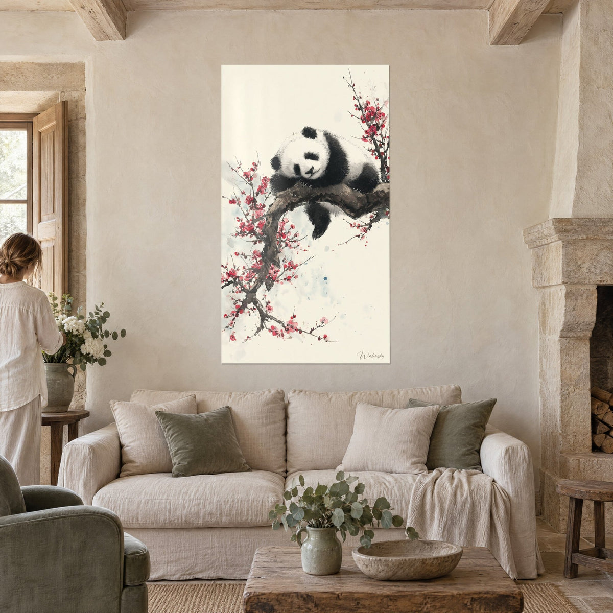 Cuadro de un panda dormido sobre su rama, flores púrpura y fondo crema, mujer de espaldas, encima de un sofá en un salón luminoso