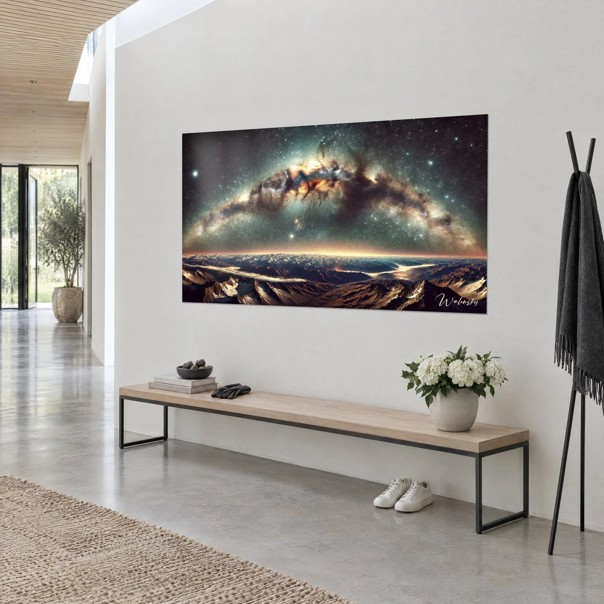 Cuadro galaxia en arco, nubes de polvo marrón y núcleo naranja, estrellas blancas, colgado en una pared clara junto a un banco de madera