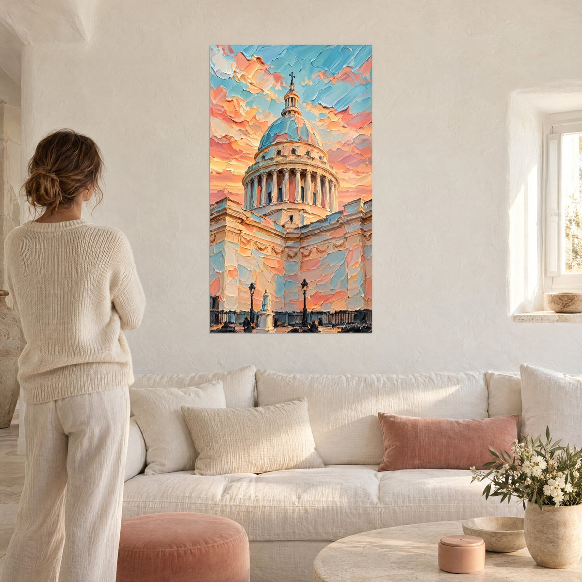 Quadro cupola del Pantheon in impasto pesca e azzurro cielo, donna di spalle con maglione color crema, sopra un divano in un soggiorno luminoso