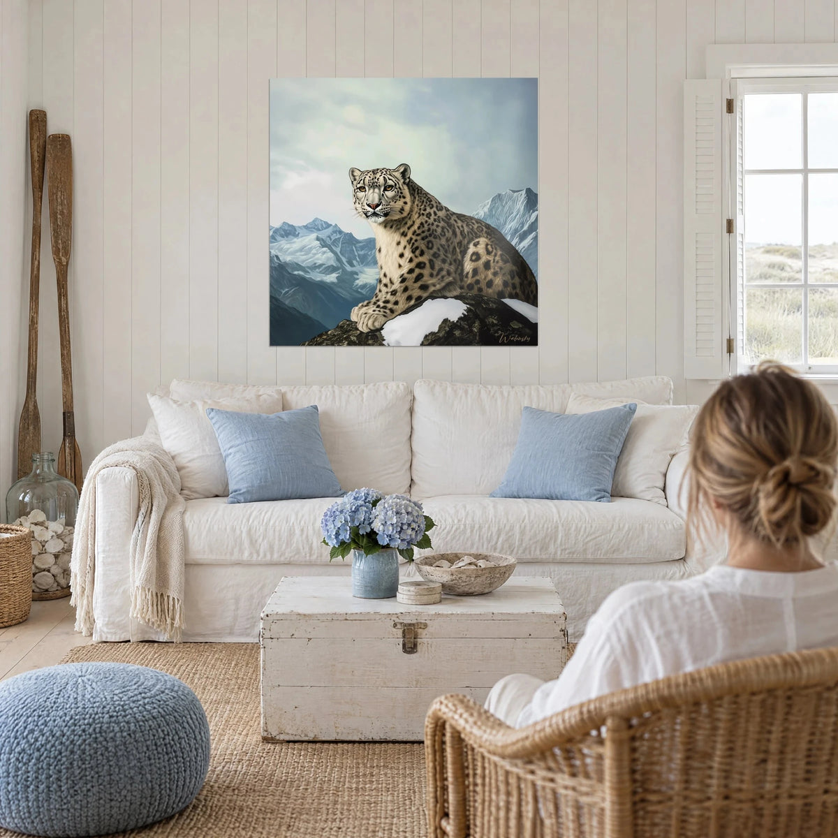 Wall art snow leopard with beige and black spotted fur, grey-blue sky, above a sofa in a bright living room