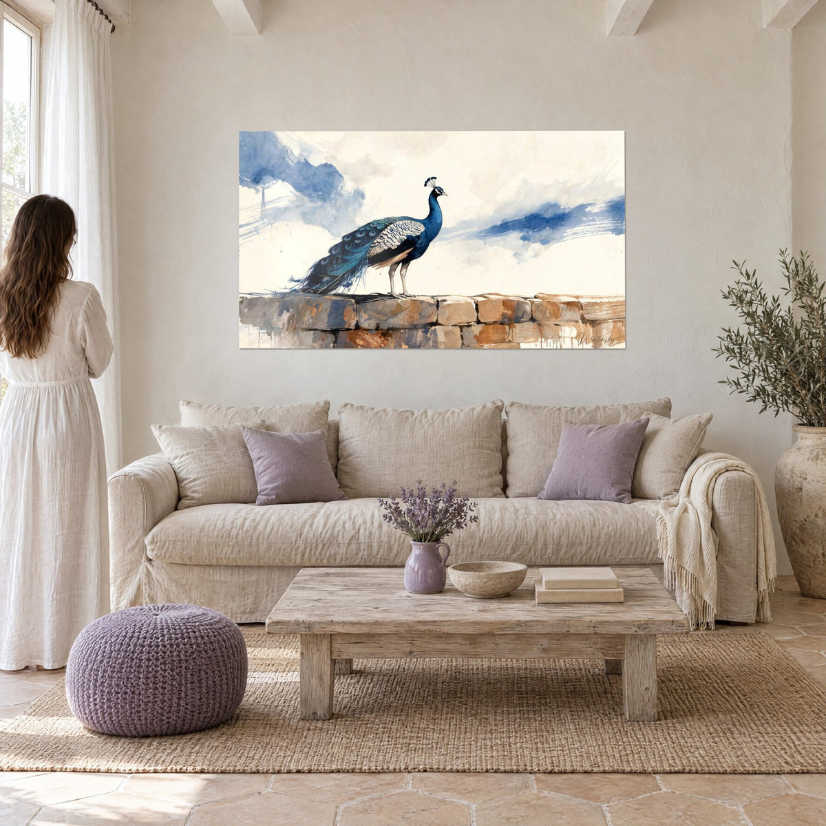 Tableau paon bleu perché sur un muret de pierre ocre, ciel crème et lavis indigo, au-dessus d'un canapé dans un salon lumineux
