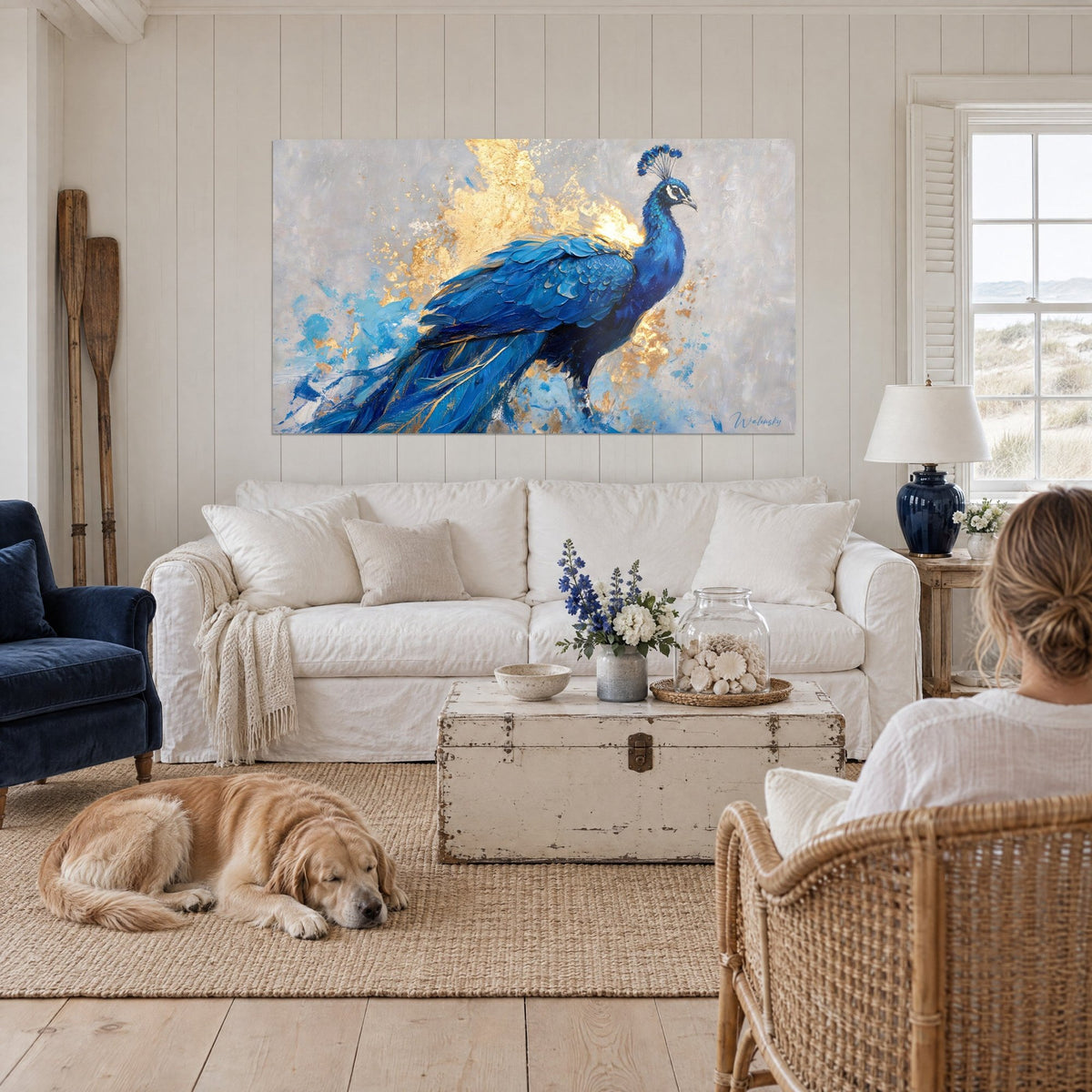 Tableau paon aux plumes bleu cobalt et éclats d'or sur fond gris perle, retriever couché, au-dessus d'un canapé dans un salon lumineux