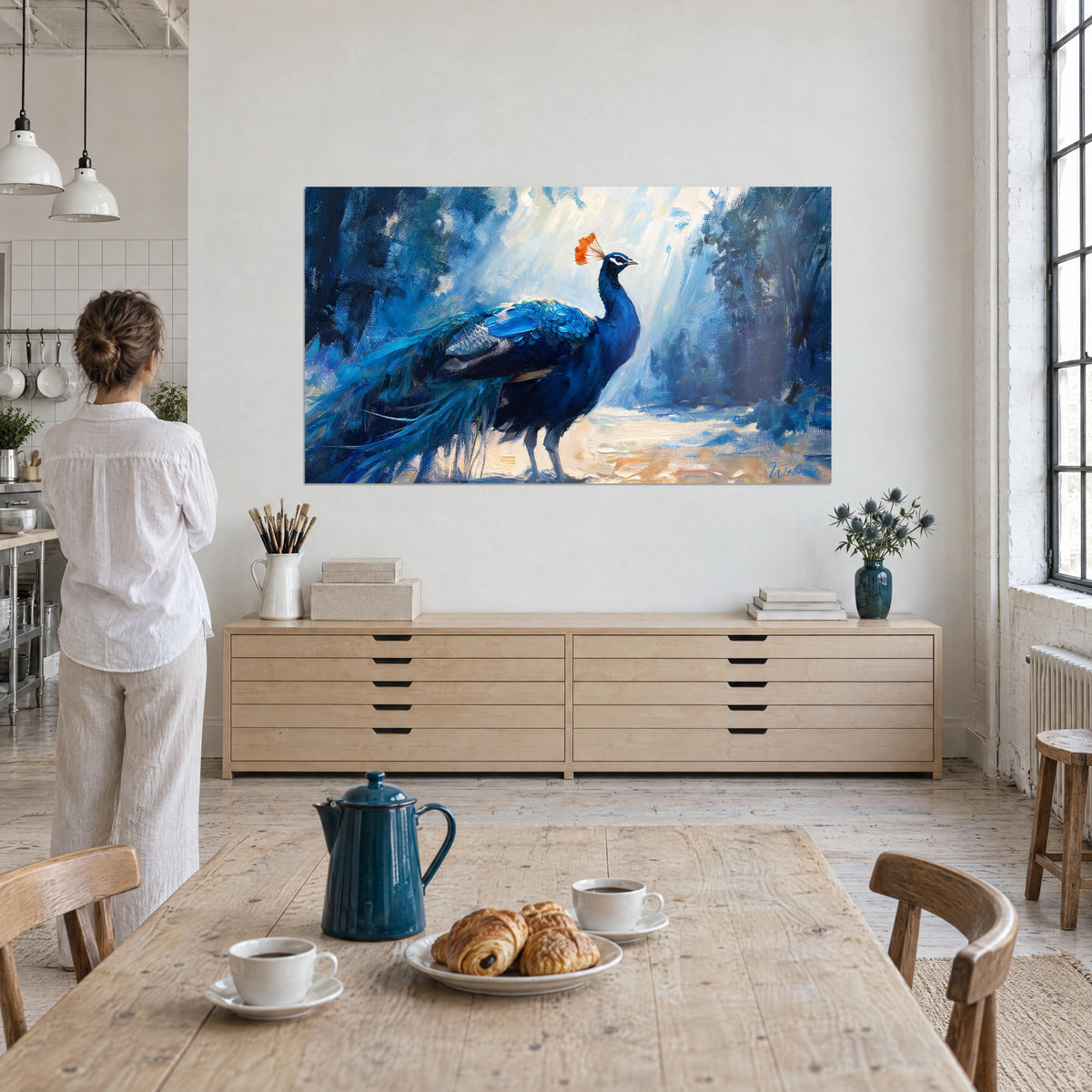 Schilderij van turquoise en kobaltblauw verenkleed met glanzende schubben, gouden zandvloer, een vrouw van achteren voor een blond houten meubel in een loft