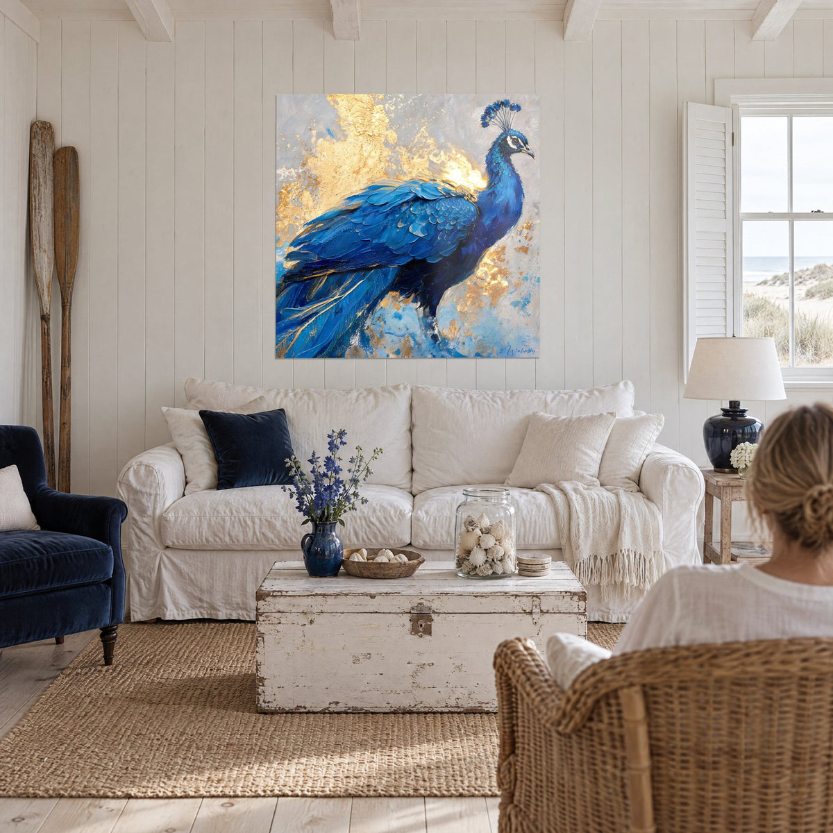 Wall art peacock in cobalt blue with thick feathers on a gold leaf background, above a sofa in a bright living room