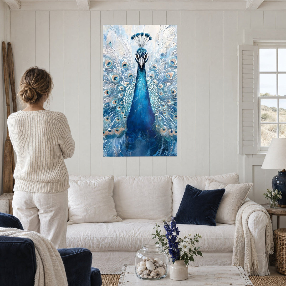 Tableau paon bleu cobalt en parade, ocelles blanches et beiges, femme de dos au-dessus d'un canapé dans un salon lumineux